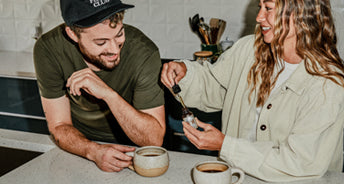 Man and woman sitting at a kitchen counter with coffee mugs.