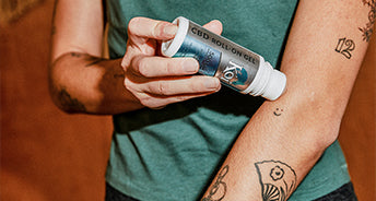 Person holding a CBD roll-on gel with visible tattoos on arms